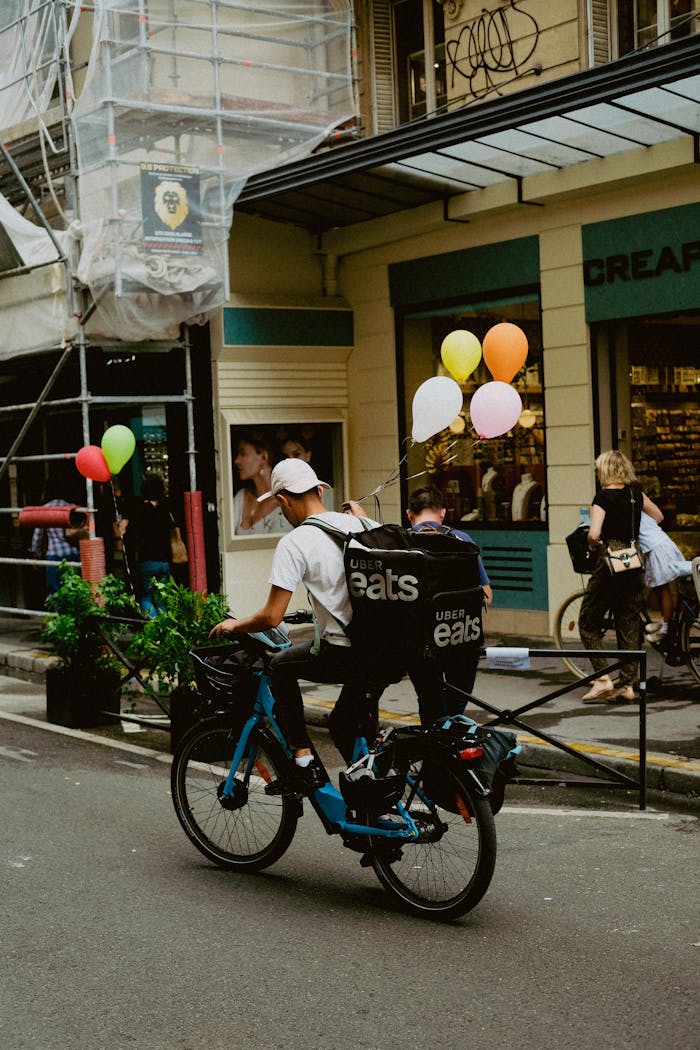 Food courier on bike with balloons, delivering in an urban setting.